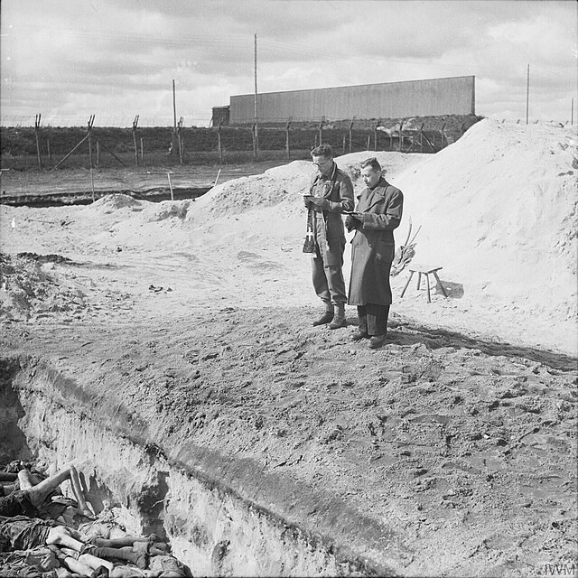Rabbi Leslie Hardman and the Roman Catholic Padre Father M C Morrison, conduct a service over one of the mass graves before it is filled in.